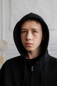Photo of sad and anxious male Caucasian teen with hoodie representing his mood before online anxiety treatment for teens in Illinois.