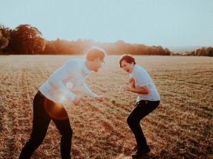 Photo of laughing Caucasian father and teenaged son playing around in an open grassy field representing one of one time spent together on the recommendation of their online anxiety therapist for kids and teens in Illinois. 