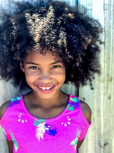 Young black girl smiling and standing near wall. Young kids are full of joy, but when anxiety in kids shows up how do you help. An anxiety therapist for specializes in online counseling for anxiety for kids can help. Helena Madsen, a child therapist ca help your child work through anxiety, stress, perfectionism, and OCD. Get in touch with Briefly Counseling today