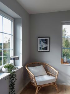 Photo of a wicker chair in the corner of a room next to a window with a plant nearby. Photo could represent a quiet place for a highly sensitive child to sit and destress from their anxiety.