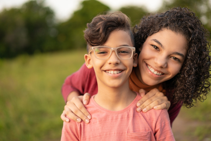 Photo of smiling Hispanic boy with glasses with his sister standing behind him also smiling and with her hands on his shoulders. Photo could represent how much hopeful this boy feels since receiving online Christian counseling for anxiety in Illinois or Florida.
